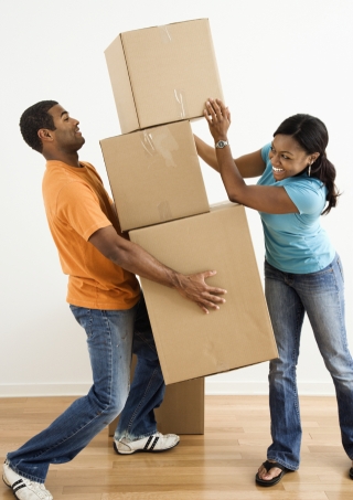 An image of African American female placing boxes on large stack man is holding.
